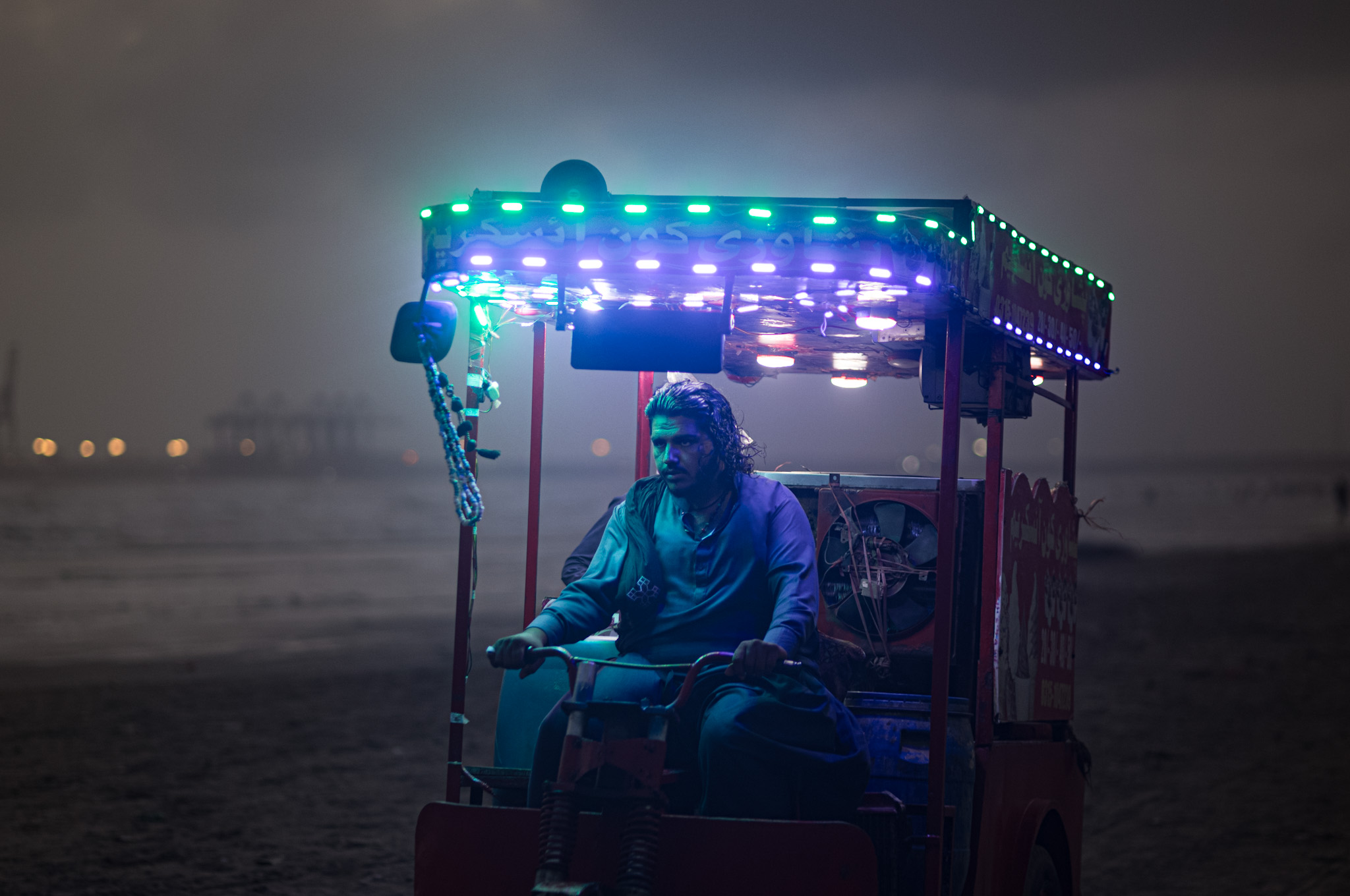 Man driving along in a colourfully-lit vehicle along the beach.