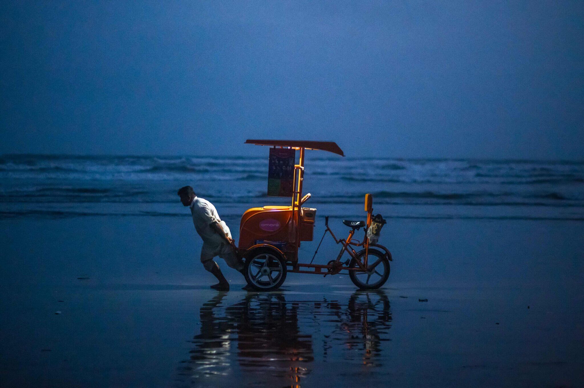 Man straining to pull a heavy cart along a beach at dusk.