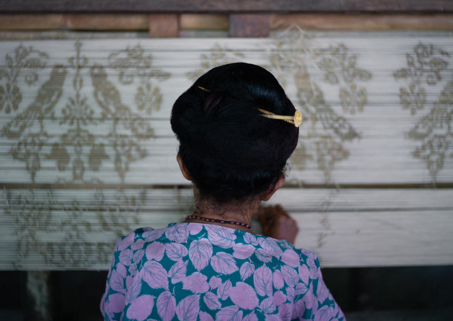 A photograph taken from behind a master woman pattern weaver