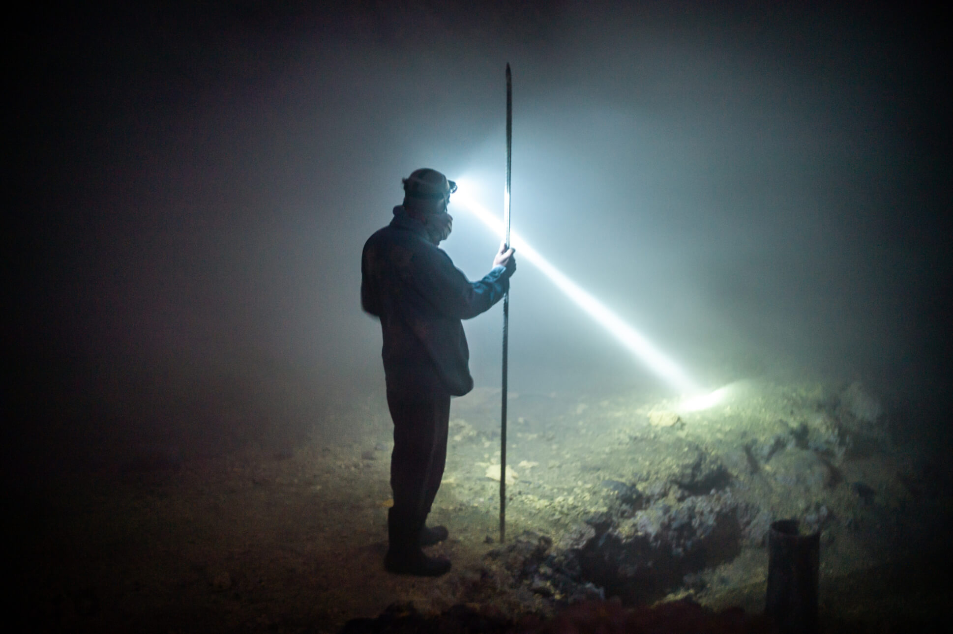 Man with a head torch looking into clouds of gas at night